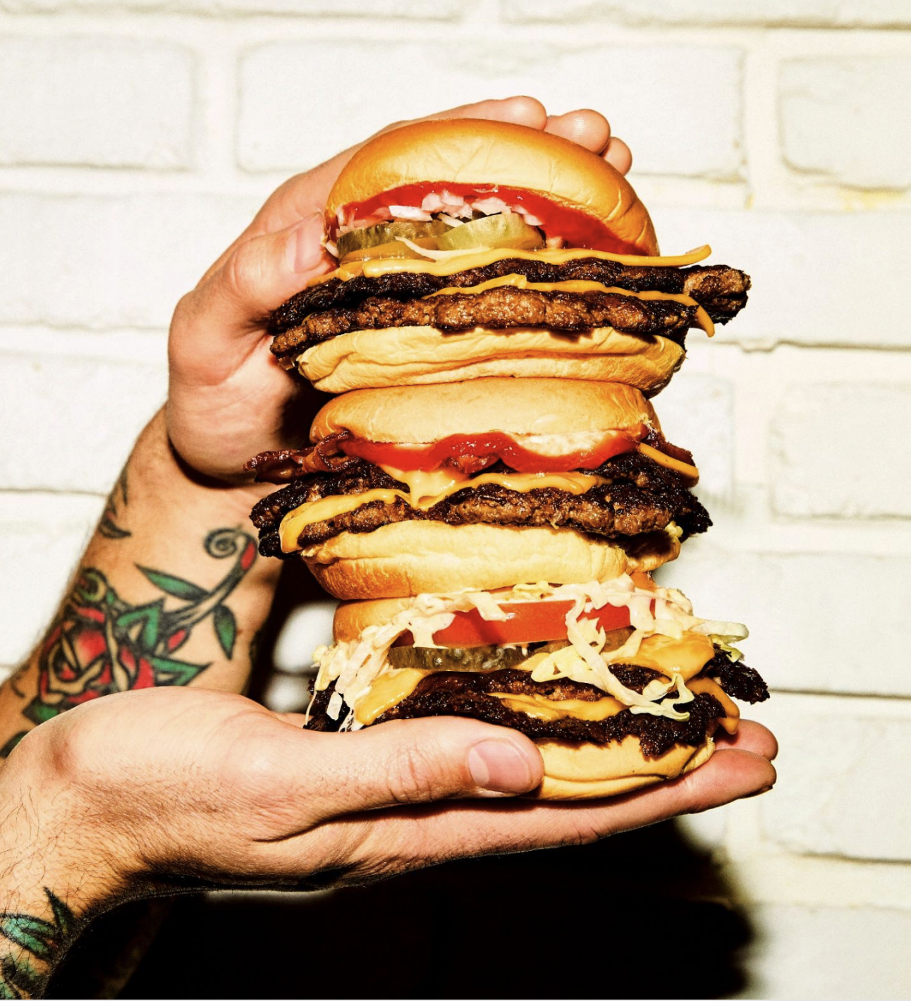 A person holding a stack of burgers